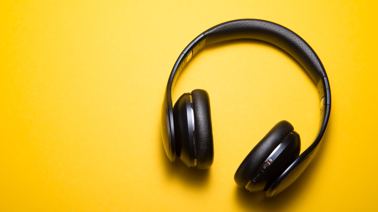 Premium over-ear headphones on a wooden desk next to a laptop and coffee