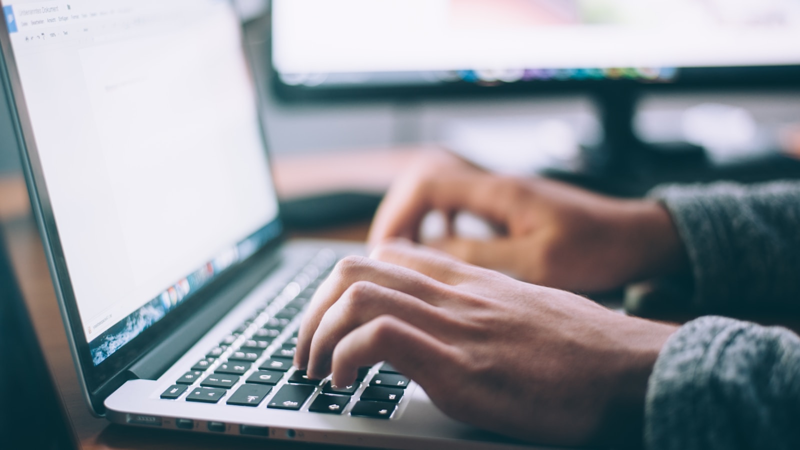 Person writing an email on a laptop next to a notebook and coffee